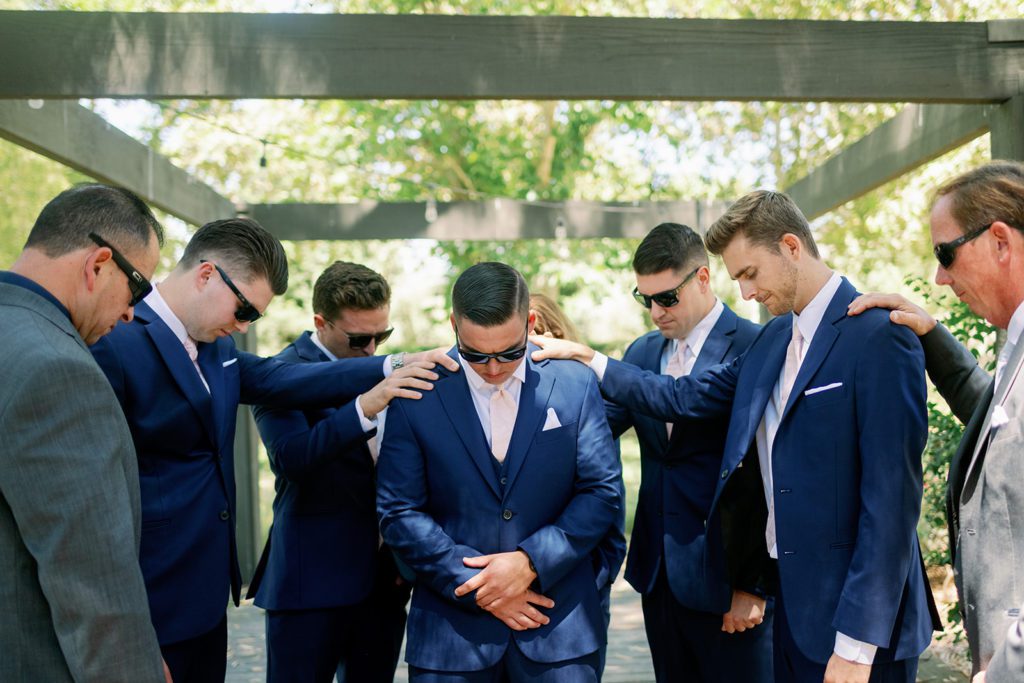 groomsmen praying over groom 